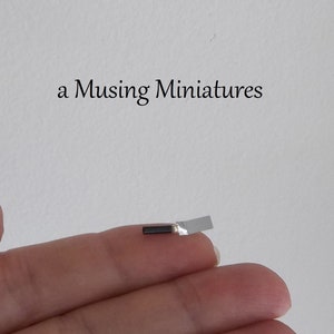 May include: A miniature black and silver trowel, held in a hand. The trowel is about the size of a fingernail.