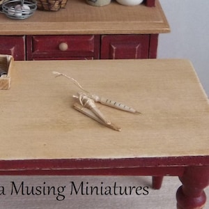 May include: A miniature wooden table with a red base and a light brown top. Two miniature carrots are tied together with twine and placed on the table.