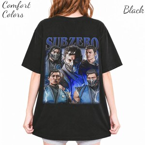 May include: A black short-sleeved t-shirt featuring a large graphic print on the back. The graphic displays five depictions of the character Sub-Zero in blue and black attire, with the text "SUB ZERO" in blue lettering above the character images.