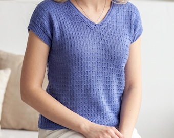 May include: A periwinkle blue short-sleeved knit top featuring a V-neckline and a vertical textured stitch pattern. The garment has ribbed trim along the sleeves and neckline, providing a structured fit with a consistent knit design throughout.