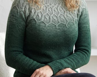May include: A long-sleeved knit jumper featuring a gradient colour transition from a deep forest green at the hem to a lighter sage green at the neckline. The yoke displays a detailed cable knit pattern that extends across the chest and shoulders.