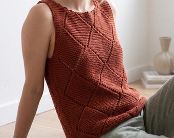 May include: A sleeveless knit top in a deep rust orange colour featuring a prominent diamond-shaped textured pattern across the front. The garment has a round neckline and wide shoulder straps, constructed with a visible garter stitch knit texture.
