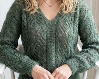 May include: A sage green long-sleeved jumper featuring a V-neckline and an intricate openwork knit pattern. The garment is constructed with a textured, semi-sheer yarn, showcasing vertical panels of lace-like detailing and ribbed cuffs at the wrists.