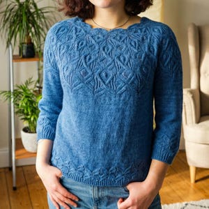Può includere: Un maglione blu lavorato a maglia con scollatura smerlata e intricati motivi testurizzati. Le maniche a tre quarti e l'orlo inferiore presentano lo stesso design dettagliato. Il maglione è realizzato con un filato morbido e di peso medio.