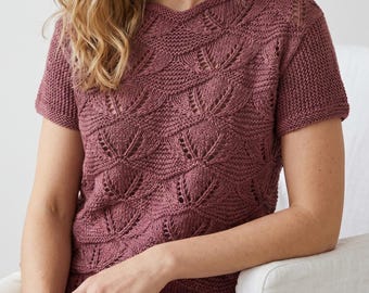 May include: A short-sleeved knit top in a dusty rose colour featuring a repeating fan-shaped lace pattern across the front. The garment has a rounded neckline and a textured stitch design that creates a series of interconnected, petal-like motifs.