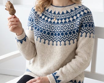 May include: A long-sleeved, crew-neck jumper in a light beige colour featuring a dark blue geometric pattern around the yoke and cuffs. The knit garment has a ribbed neckline, cuffs, and hem, showcasing a detailed, repeating motif of diamonds and stylized shapes across the chest and shoulders.