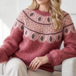 Può includere: Un maglione in maglia a maniche lunghe color rosa polvere con scollo rotondo e polsini a coste. Il carré presenta un motivo decorativo in pizzo traforato rosa chiaro, accenti scuri a forma di diamante e sottili linee metalliche orizzontali.