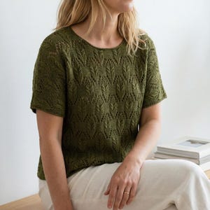 May include: Olive green short-sleeved knit top with a round neckline. The top features a detailed leaf pattern throughout the fabric. The model is wearing the top with light-coloured trousers. The top is a comfortable and stylish garment.