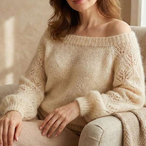 Peut inclure: Pull-over crème clair à épaules dénudées et manches longues. Le pull présente un motif en tricot texturé et une encolure large. Les manches ont un léger effet bouffant aux épaules et sont resserrées aux poignets. Le pull est en matière douce et duveteuse.