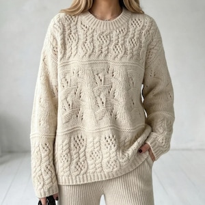 May include: A white ceramic mug with a black handle and the text "But First, Coffee" in a bold, black font. The mug is set against a blurred background, suggesting a cozy setting.