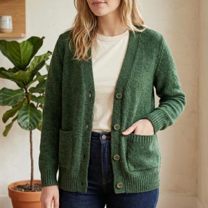May include: A green cardigan sweater with a V-neck, button closure, and two front pockets. The sweater is made of a textured knit fabric and is worn over a white t-shirt and blue jeans.