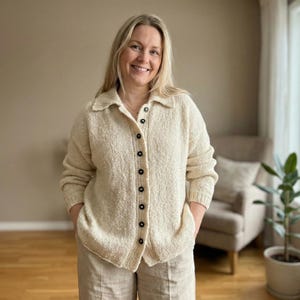 May include: A cream-colored button-down cardigan with a textured knit design. The cardigan has a collared neckline and is buttoned up. The person is wearing beige pants. The cardigan is a neutral color and can be worn in many settings.