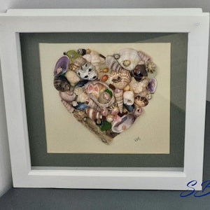 May include: A framed artwork featuring a heart-shaped arrangement of various seashells. The shells, in shades of white, brown, and purple, are set against a light beige background. The white frame adds a clean, modern touch to this coastal-themed piece.