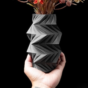 May include: A white ceramic mug with a black handle and the text "But First, Coffee" in a black, bold font. The mug is on a white surface. The mug is approximately 10 cm tall.