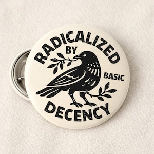 May include: A round, off-white button with the text "RADICALIZED BY BASIC DECENCY" in black. A black bird with a sprig in its beak is in the center. A second button is partially visible.