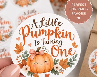 May include: A round white sticker featuring the text A Little Pumpkin Is Turning One in brown and orange script. The design includes a smiling orange pumpkin with a pink bow, surrounded by autumn leaves, small flowers, and tiny orange hearts.