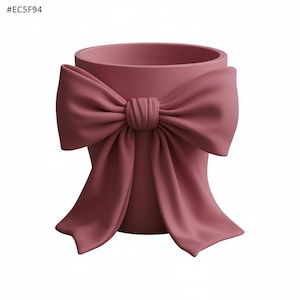 May include: A dusty rose-colored planter with a large bow detail. The bow is sculpted to appear as if it's made of fabric, adding a soft, feminine touch to the ceramic pot. The planter has a cylindrical shape.
