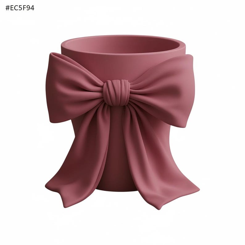 May include: A dusty rose-colored planter with a large bow detail. The bow is sculpted to appear as if it's made of fabric, adding a soft, feminine touch to the ceramic pot. The planter has a cylindrical shape.
