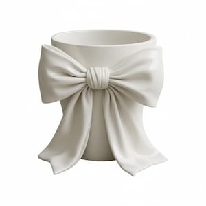 May include: A white ceramic vase with a large, sculpted bow detail. The bow is centered on the vase and has flowing ribbons. The vase has a cylindrical shape and a smooth, glossy finish. The overall design is elegant and decorative.