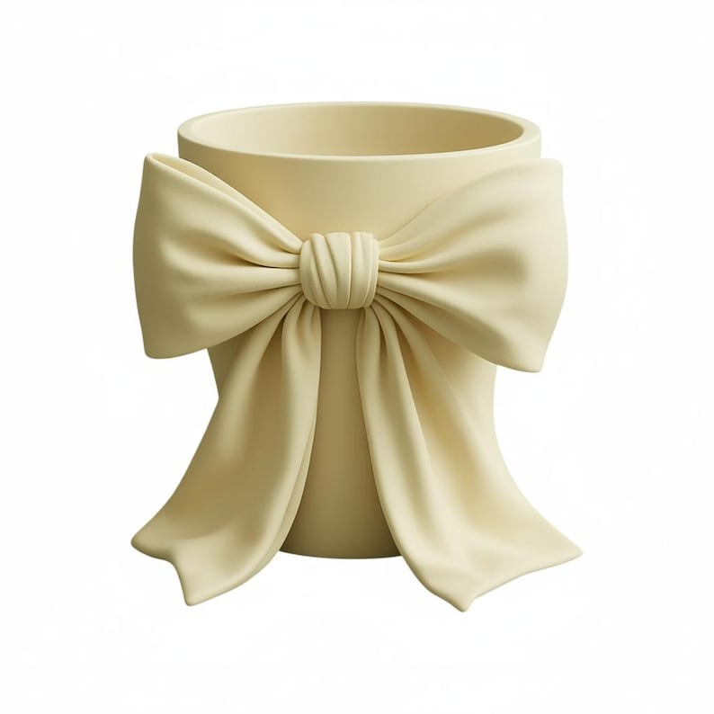 May include: A cream-colored decorative vase with a large bow design. The bow is centered on the vase and has flowing fabric-like details. The vase has a cylindrical shape with a wide opening.