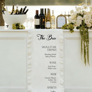 以下が含まれることがあります： ワインボトル、グラス、そして「The Bar」と書かれた看板がある白いバー。看板には、ドリンク、ワイン、ビール、スピリッツがリストされています。緑のブドウと白い花がバーを飾っています。