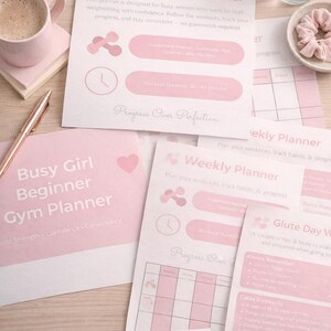 May include: A selection of pink and white fitness planners, a coffee cup, and accessories on a wooden surface. The planners include workout guides and tracking sheets. Other items include glasses, a pen, and wireless earbuds.