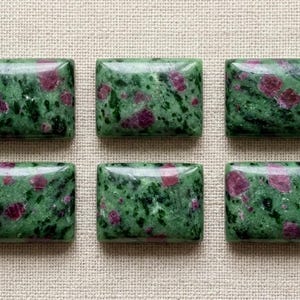 Puede incluir: Seis cabujones rectangulares de zoisita con inclusiones de rubí, dispuestos en dos filas de tres. Cada piedra pulida presenta una base verde moteada con motas minerales negras oscuras y parches de rubí rosa magenta opaco.
