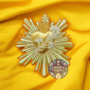 May include: Embroidered gold Sacred Heart patch with a cross and floral accents. The patch features a gold heart with a crown of thorns, surrounded by rays of light. The patch is on a yellow background. The text "Liturgical Elegance" is in a circle.