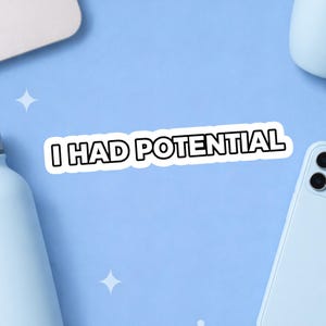 May include: A white sticker with the text "I HAD POTENTIAL" in black letters with a white border. The sticker is on a light blue surface, with a laptop, phone, and water bottle in the background.