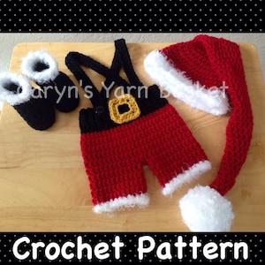 Può includere: Completo da Babbo Natale all'uncinetto per un bambino, che comprende un cappello rosso e bianco con una lunga coda bianca, pantaloni rossi e neri con una fibbia dorata e scarpette nere.