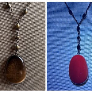 May include: A long necklace with a dark metal chain and a large, oval pendant. The pendant is a dark brown color with a lighter brown interior. The chain has small, round beads and a Y-shaped design at the top.