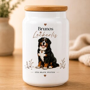 Könnte beinhalten: Ein weißer Keramikbehälter mit Holzdeckel, verziert mit einer Illustration eines Berner Sennenhundes. Der Text lautet Brunos Leckerlis und FÜR BRAVE PFOTEN, ergänzt durch kleine Herz- und Blumenmotive. Das Design ist mittig auf der Vorderseite.