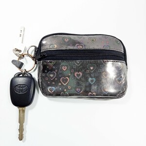 Peut inclure: Petite pochette argent&eacute;e avec fermeture &eacute;clair noire et motif c&oelig;urs. Un porte-cl&eacute;s avec une cl&eacute; de voiture et une cl&eacute; de maison est attach&eacute;. La pochette est con&ccedil;ue pour contenir de petits objets comme des cl&eacute;s, des cartes ou de l'argent.