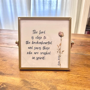 May include: Square gold-framed print with the text "The Lord is close to the brokenhearted and saves those who are crushed in spirit." A watercolor flower illustration is on the right. Psalm 34:18 is written at the bottom.