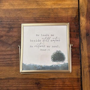 May include: A gold-framed picture with a watercolor background and a quote from Psalm 23: "He leads me beside still waters. He restores my soul."