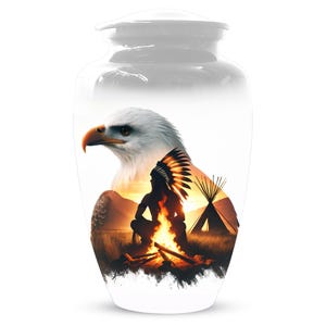 May include: A white cremation urn with a design depicting a bald eagle, a Native American figure, a campfire, and a teepee against a sunset. The urn has a lid and a rounded shape, suitable for ashes.