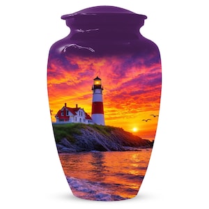 May include: A purple cremation urn with a glossy finish. The urn features a scenic image of a lighthouse on a rocky coast at sunset, with a red and white striped tower, a red-roofed house, and a vibrant orange sky.