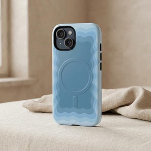May include: A light blue smartphone case featuring a wavy, layered pattern in various shades of blue. The case includes a circular MagSafe magnetic charging ring on the back and a black camera module cutout at the top left corner of the device.
