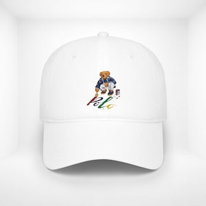 May include: White baseball cap featuring a cartoon bear in a painter's outfit, with the word "Polo" in colorful script. The bear is holding a paintbrush and a paint can. A classic, casual accessory.