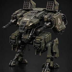 Puede incluir: Un mecha de combate táctico de color verde oliva con lanzadores de misiles dobles montados en los hombros, dos cañones giratorios laterales y una cabina central con el texto XM-03 impreso en el frente. La unidad mecánica tiene patas articuladas.