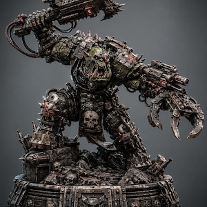May include: A green-skinned orc warrior figurine in heavy, weathered dark metal armour with spikes and skull motifs. The figure holds a large mechanical chain-axe overhead and features a clawed mechanical hand, standing on a detailed base.