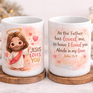 May include: Two white ceramic mugs featuring a cartoon illustration of Jesus with a halo, pink hearts, and the text Jesus Loves You. The other side displays the text As the Father has loved me, so have I loved you. Abide in my love. John 15:9.
