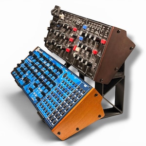 May include: A dual-tier synthesizer stand holding two analog synthesizers. The top unit is black with red and blue knobs, while the bottom unit features a blue faceplate with numerous black knobs and patch points, supported by wooden side panels.