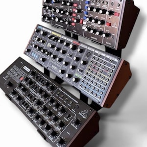 May include: Three black Behringer synthesizers stacked vertically on a stand. The top unit is a Model D, the middle is a Model 15, and the bottom is a Poly-800. Each unit features numerous black control knobs, switches, and input/output ports.