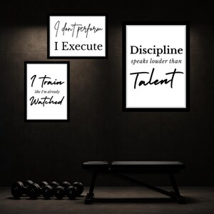Może przedstawiać: Trzy oprawione plakaty motywacyjne z czarnymi ramkami i białym tłem. Plakaty wyświetlają frazy "I don't perform, I execute", "Discipline speaks louder than Talent" i "I train like I'm already watched". Ławka do ćwiczeń i hantle znajdują się na pierwszym planie.