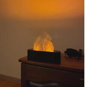 May include: A black, oval-shaped electric fireplace with a flame effect. The flames are bright orange and yellow, and the unit sits on a wooden surface. The background is a warm, orange gradient.