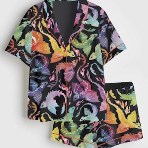 May include: Black pajama set with a colorful dragon pattern. The short-sleeved top and shorts feature a repeating design of rainbow-colored dragons with orange trim. The set is made of a soft, comfortable material.