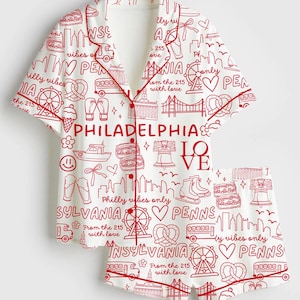 May include: White pajama set with red trim and a repeating red pattern of Philadelphia landmarks and phrases. The set includes a short-sleeved button-up shirt and matching shorts. The words "PHILADELPHIA LOVE" are prominently displayed.