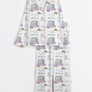 K&ouml;nnte beinhalten: Wei&szlig;es Pyjama-Set mit einem sich wiederholenden Muster aus rosa Golfwagen, Hunden und Golfplatzelementen. Das lang&auml;rmlige Oberteil und die Hose haben eine rosa Bord&uuml;re. Das Pyjama-Set ist aus einem weichen, leichten Stoff gefertigt.