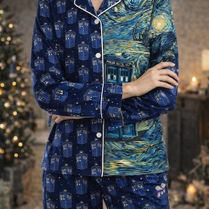 May include: Navy blue pajama set featuring a split design. One side showcases a pattern of blue police box graphics, while the other side depicts a starry night scene. The set includes a button-down top and matching pants.